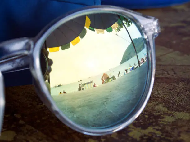 Sunglasses on table reflect beach with sea views and sunny holiday weather.