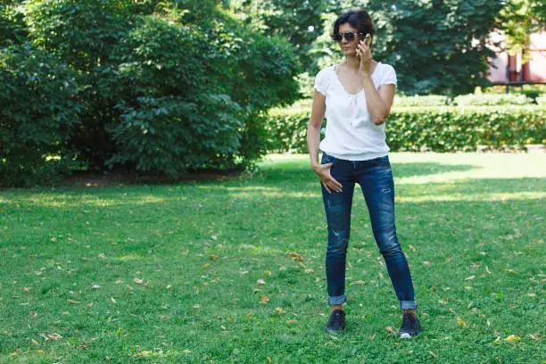 The brunette girl in the park . A concept of calm mood and relaxation in a park on the green grass. A middle-aged woman in blue jeans.