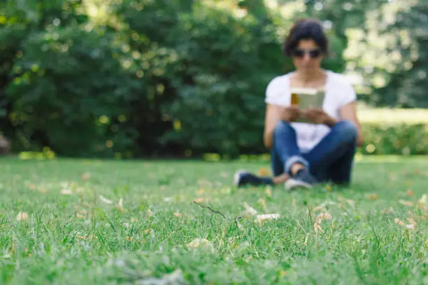 A girl is reading in the park. A concept of calm mood and relaxation in a park on the green grass. A middle-aged woman in soft focus.