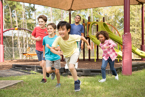 Multi-ethnic group of school children playing on school playground.  The group of friends excitedly run toward the next outdoor activity.  Education in USA, exercise themes.