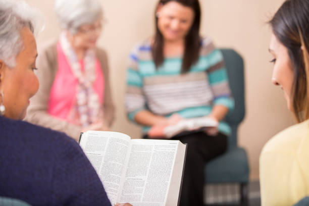 Multi-ethnic, mixed age bible study group. Multi-ethnic, mixed age group of people involved in Christian bible study meeting at local church. Senior adult woman leads group. church ladies stock pictures, royalty-free photos & images