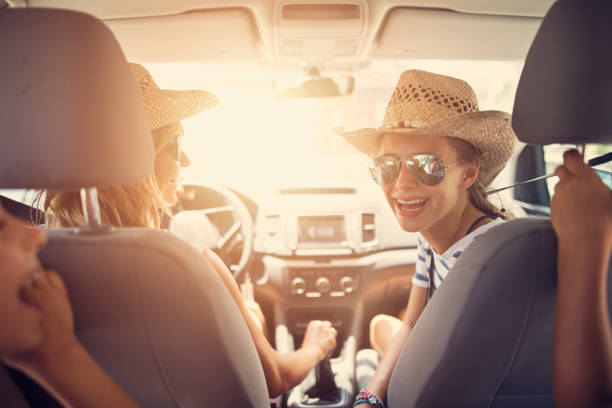 Family having fun travelling by car. Mother id driving and teenager daughter is laughing at the brothers on back seat.\nNikon D850