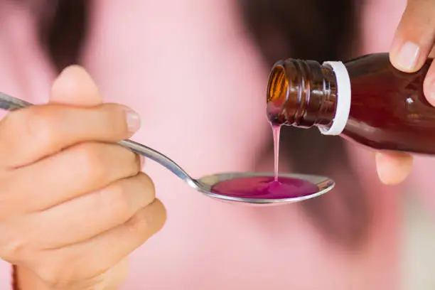 Photo of Woman hand pouring medication or antipyretic syrup from bottle to spoon. healthcare, people and medicine concept.