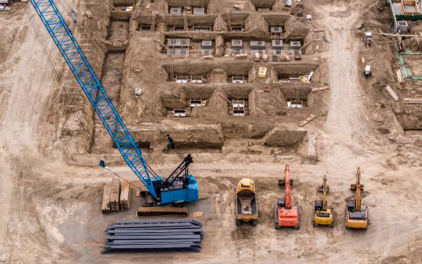 Blue Crane, Yellow Dumptruck, Orange Excavator working on building a foundation Drone view of busy construction site where foundation building is in progress big blue crane stock pictures, royalty-free photos & images