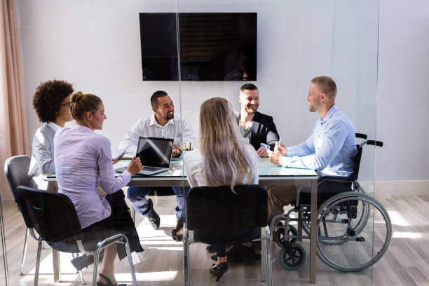 Disabled Manager Sitting With His Colleagues Disabled Male Manager Sitting With His Colleagues At Workplace wheelchair photos stock pictures, royalty-free photos & images