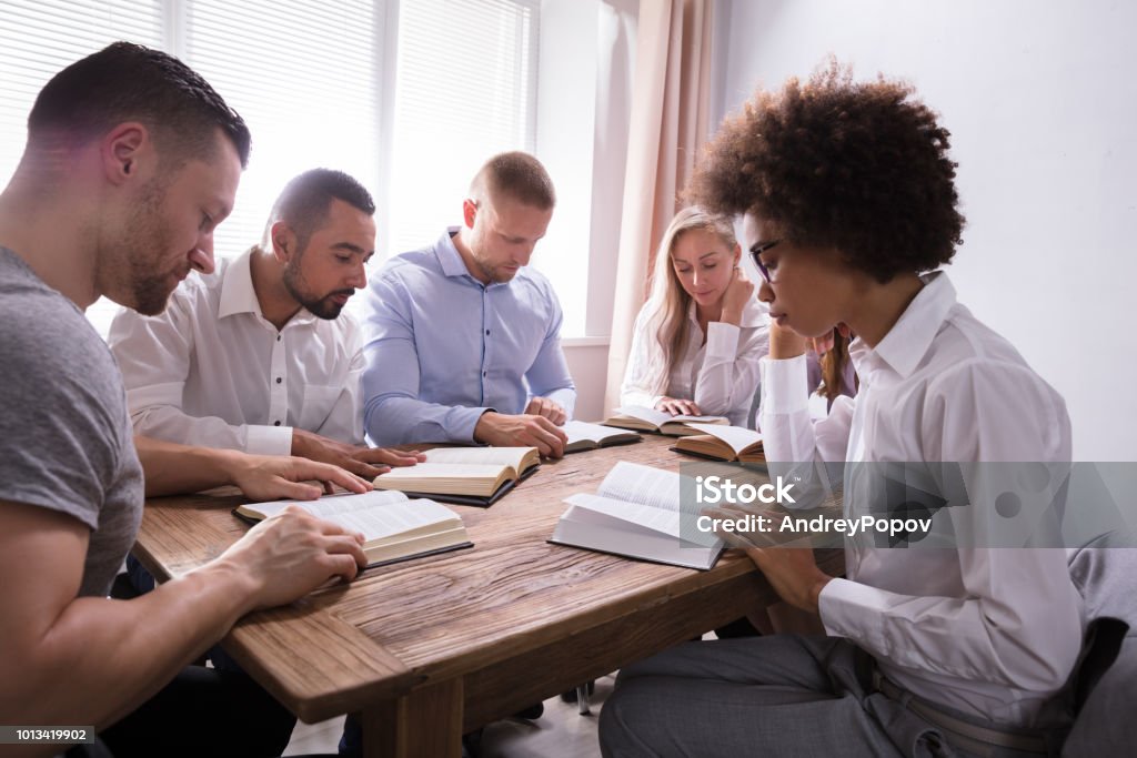 Group Of Young Multiethnic People Reading Bible Group Of Young Multiethnic People Reading Bible Over Wooden Desk Bible Stock Photo