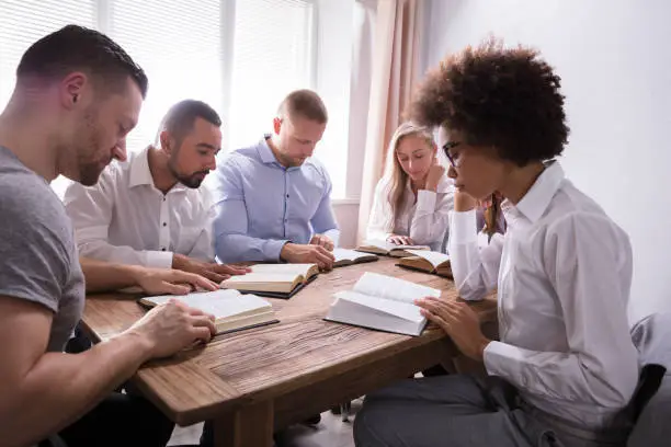 Group Of Young Multiethnic People Reading Bible Over Wooden Desk