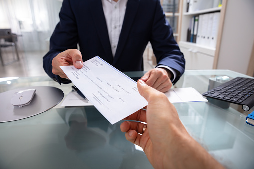 Businessman's Hand Giving Cheque Over Glass Desk
