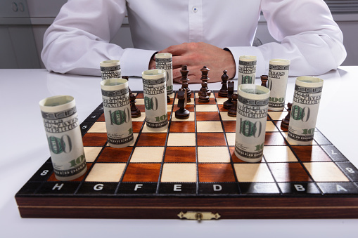 Businessman Playing Chess With Chess Piece And Rolled Up American Banknotes
