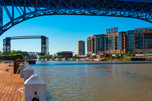Cleveland, OH, USA - May 25, 2018: The recently developed Flats East Bank entertainment complex rises on the Cuyahoga River as seen from the west bank, with the Main Avenue highway bridge overhead.