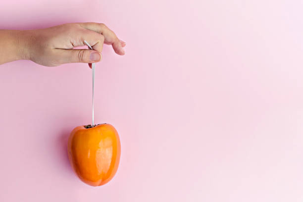 istock Female Hand holds hanging ripe persimmon on ribbon 1013455268