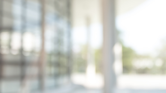 Office or university building blur background exterior view with blurry empty lobby space, entrance hall glass wall window and light bokeh