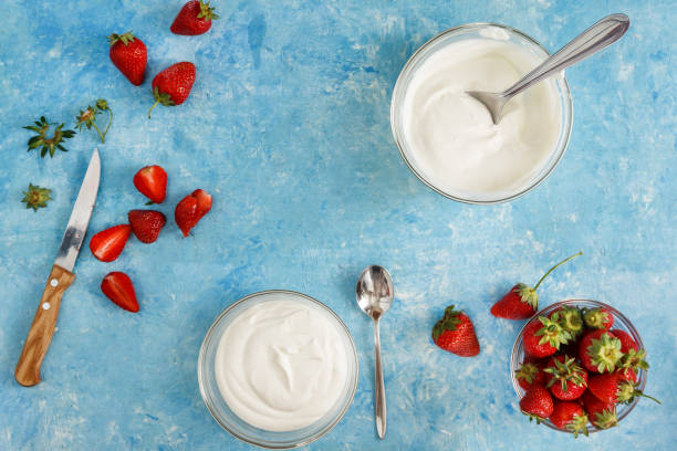 Organic yogurt in a bowl with freshly cut strawberries on a blue coOrganic yogurt in a bowl with freshly cut strawberries on a blue concrete background. Top view and close-up. Flatlay stock photo