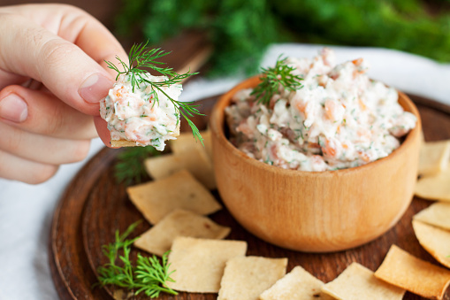 Smoked salmon, cream cheese and dill dip in wooden bowl served with gluten free crackers on round cutting board