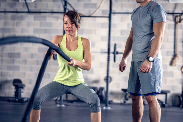 istock Fit woman swinging battle ropes under coach supervision 1013461020