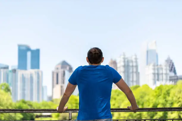 Photo of Young man standing leaning on railing in Piedmont Park in Atlanta, Georgia with scenic cityscape skyline of urban city skyscrapers downtown, Lake Clara Meer