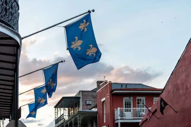 New Orleans old town Bourbon street in Louisiana famous town, city, blue flags hanging off balcony wall, nobody at dark evening sunset, architecture, clouds in sky