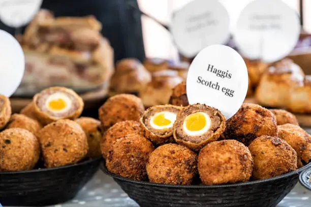 Closeup bowl of Haggis Scotch deep fried eggs with sign in market street food fair, cross section cut open, yellow yolk, breading tradition English food in London, United Kingdom