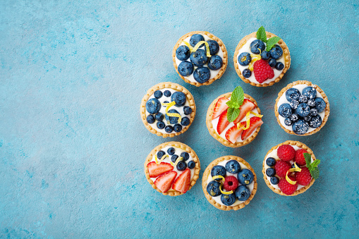 Tartlets or cake with cream cheese and berry on turquoise table from above. Сolorful pastry dessert.
