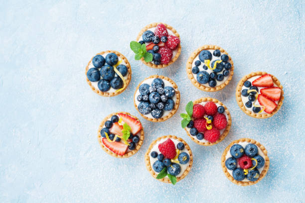 tavolo blu decorato con zucchero in polvere con crostate di bacche di varietà o vista dall'alto della torta. dolci di pasticceria. - little cakes foto e immagini stock