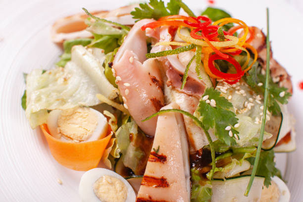 istock Caesar salad with quail eggs, cherry tomatoes, Parmesan cheese and grilled calamari, octopus in white plate on light table. 1013515232