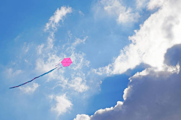 One pink kite flying over a cloudy sky