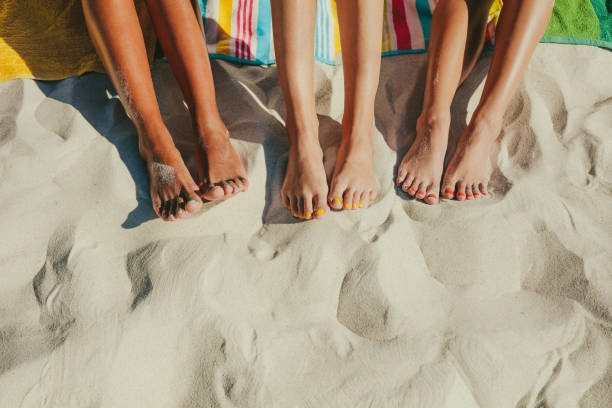 Close up of legs of three women at the beach Close up shot of legs of three women sitting on the beach with nails painted in different colours. toe stock pictures, royalty-free photos & images