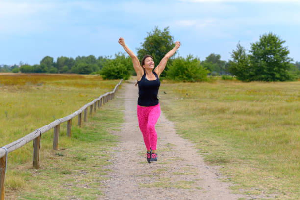 Side view of woman running through green forest wearing sportswear and headphones. Outdoor cardio training