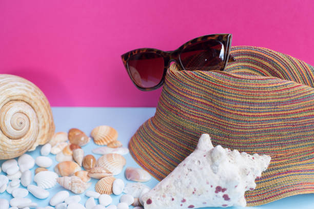 istock A women's sunglasses over a large sea-bream and several smaller shells on a light blue and fuchsia background 1013550120