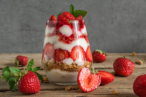 strawberry yogurt parfait with granola, mint and fresh berries in a glass on rustic wooden table. delicious healthy food. close up