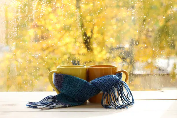 mugs tied together warming scarf on the background of a wet window after the rain