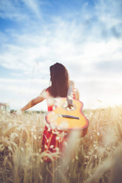 istock Woman walking through the wheat field with guitar on back. 1013631730