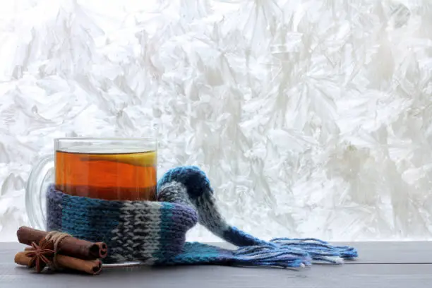 lemon tea in a transparent mug with a warm scarf and cinnamon sticks against the window with frosty patterns