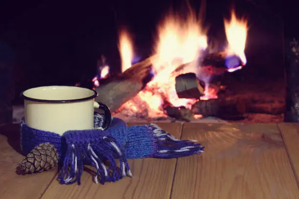 metal mug of mulled wine wrapped in a scarf on the background of the fireplace