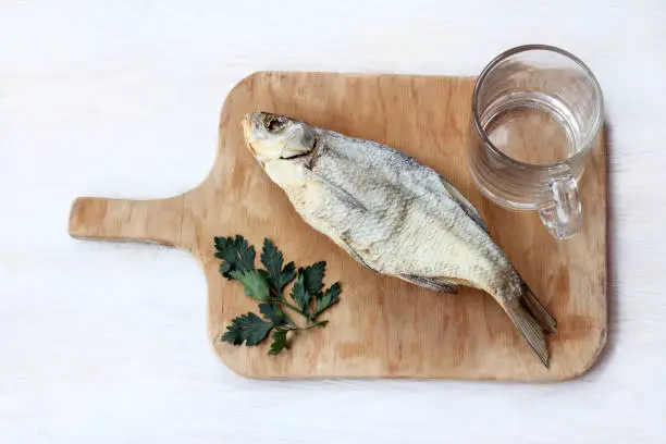 flat layout of Dried fish with parsley and empty transparent glass on a wooden plank