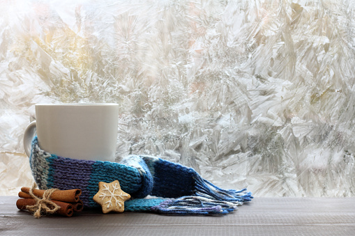 large white mug with blue scarf standing on a table with cinnamon and ginger cookies