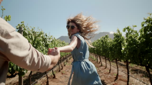 Young couple running through grape vines holding hands