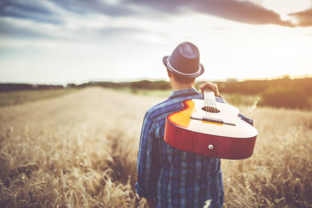 istock Man walking through the wheat field with guitar on back. 1013640120