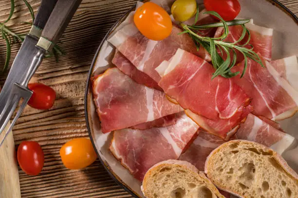 Thinly sliced German black forest ham with sliced ciabatta bread, tomato and olives.