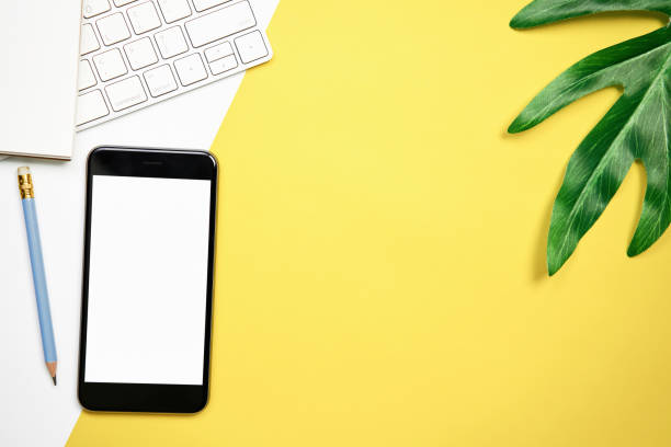 istock Blank screen smartphone and keyboard with note pad placed on yellow background. Suitable for graphics used for advertising. 1013683562
