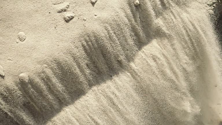 White fine sand avalanche slopes down the hill under sun light. Closeup view. Slow motion