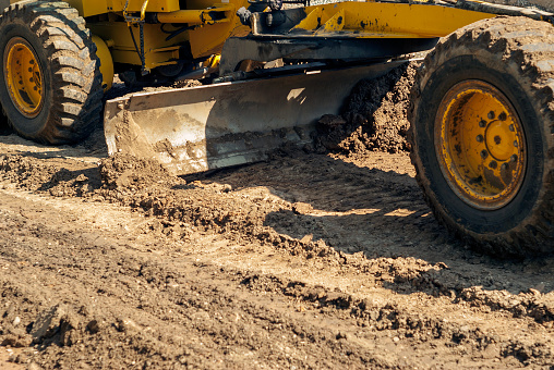 closeup - the blade of a motor grader in the process of leveling a sandy road foundation