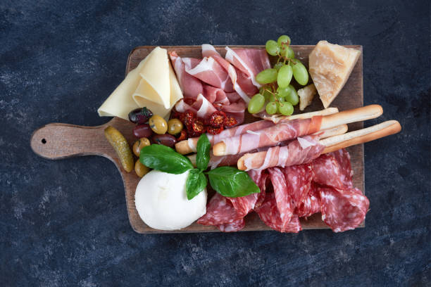 set de vin italien antipasti de collations. brushettas, variété de fromages, olives méditerranéennes, cornichons, jambon de parme avec melon, charcuterie et vin dans des verres sur fond grunge noir, vue de dessus - entrée italienne photos et images de collection