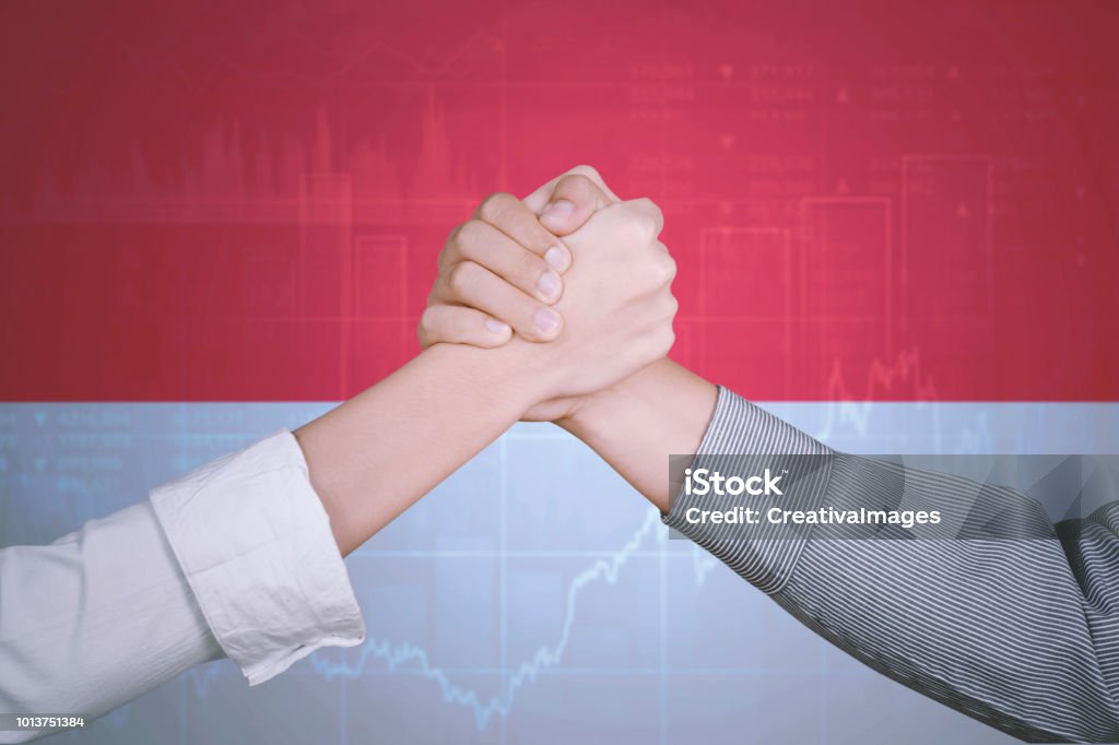 Successful handshake with Indonesia flag Closeup of two business partners shaking hands to celebrate their success near a growth chart and Indonesia flag Achievement Stock Photo