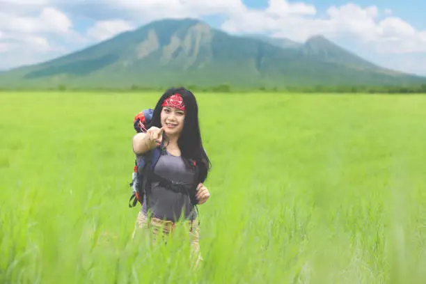 Portrait of a beautiful woman pointing at you while standing in the meadow with mountain background