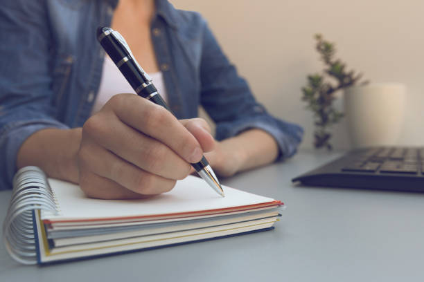 Woman's hands with pen writing on notebook. Modern grey office desk. Working, writing concept