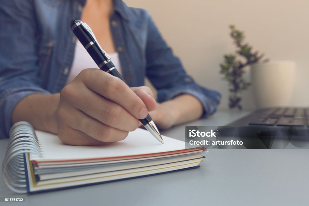 Woman's hands with pen writing on notebook. Modern grey office desk. Working, writing concept Diary Stock Photo