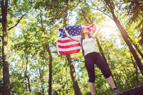 istock Woman with backpack holding american flag in forest. 1013760508