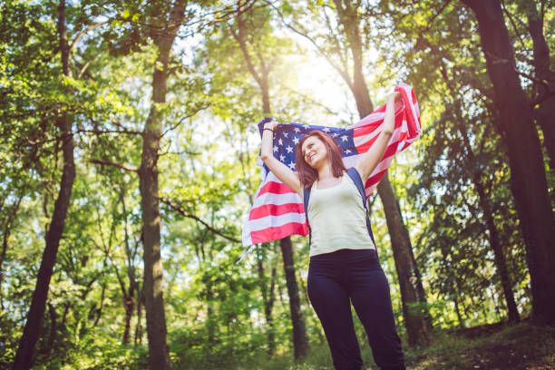 istock Woman with backpack holding american flag in forest. 1013761848