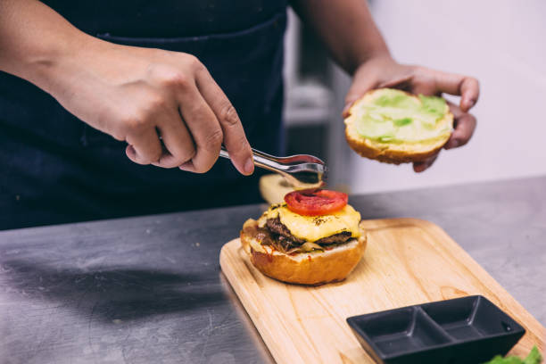 istock Chef add a sliced of tomato for making a beef cheeseburger on wooden plate. 1013765718